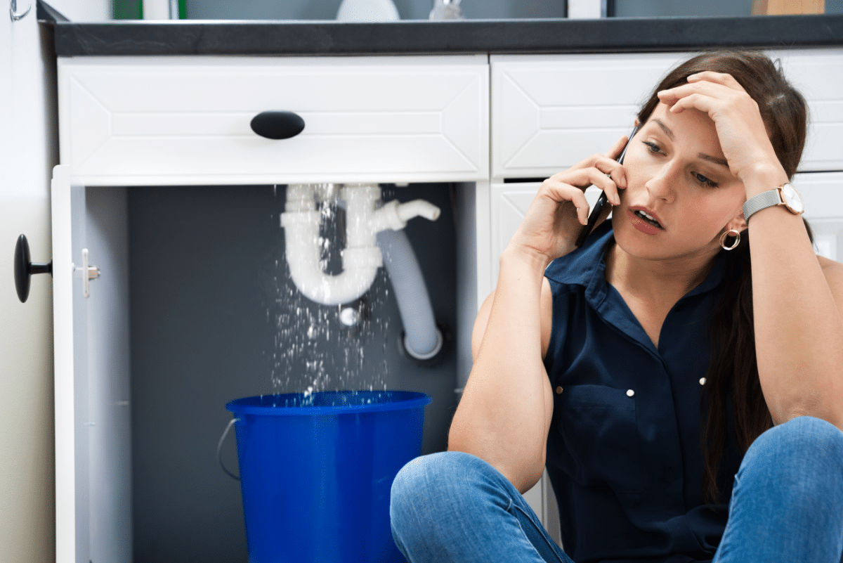 Women sitting in her kitchen in distress with the sink leaking