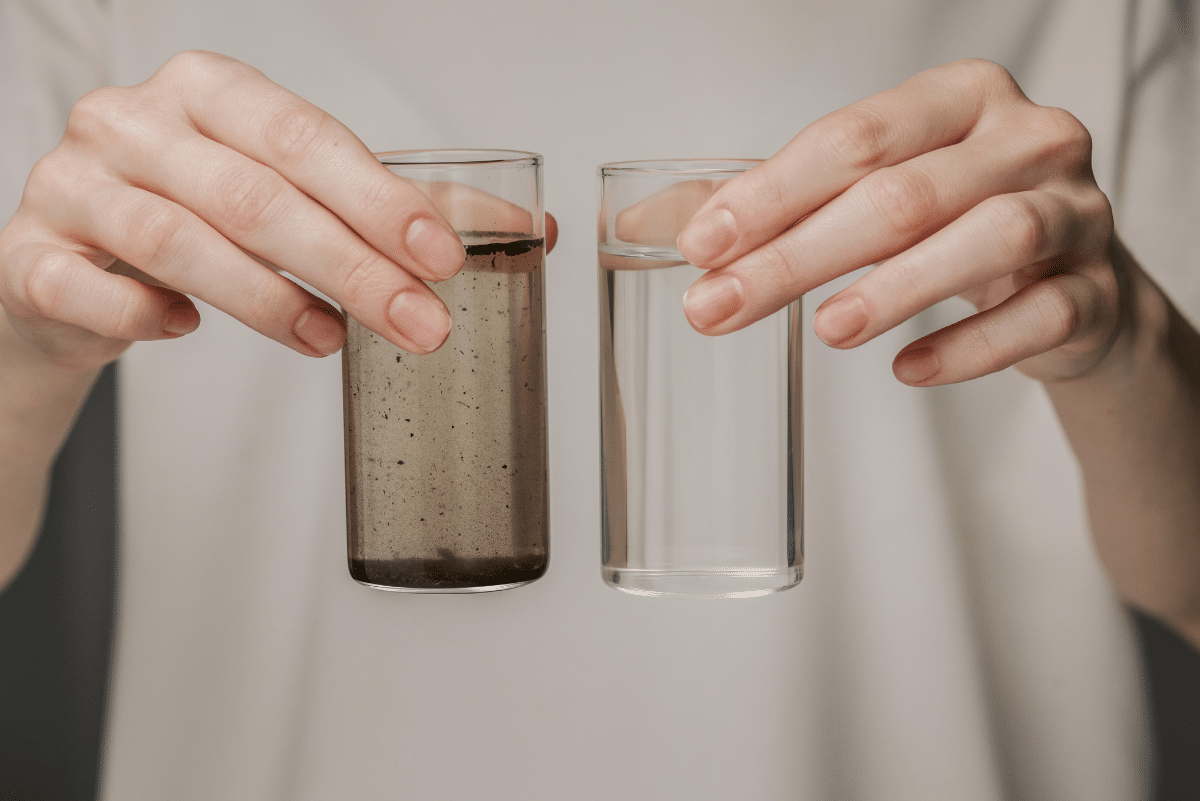 Person holding one dirty cup of water and one clean cup of water